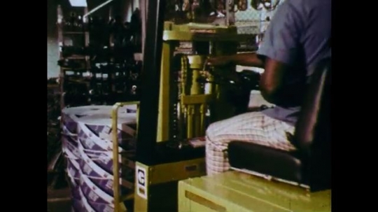 1970s: UNITED STATES: man drives truck in warehouse. Truck moves boxes. Man takes off gloves. Trucks collide