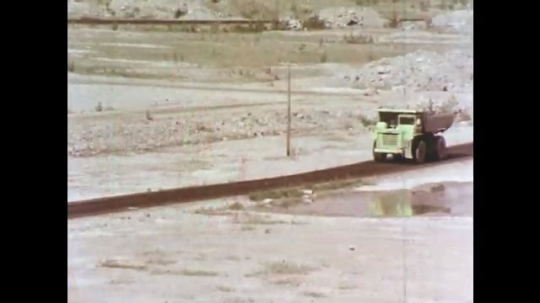  1970s: Dirt and rocks fall from backhoe bucket.  Dump truck drives on dirt road through industrial facility.  Conveyer belt.
