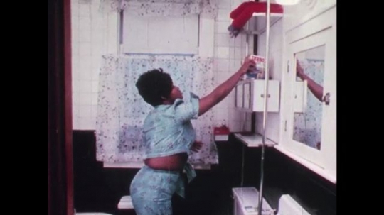 1970s: UNITED STATES: lady puts cleaning products on high shelf. Lady moves plant from ground to shelf