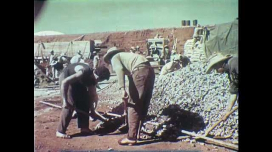1950s: Construction site.  Men use shovels.  Men carry loads of rocks in teams.  Workers.  Cement mixers.
