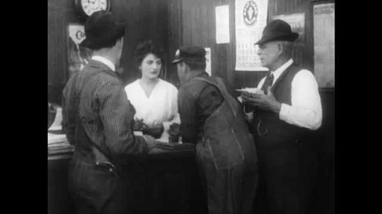 1910s: Man struggles against two other men. Woman leans in and points at struggling man, man bows and walks off. One of the other men turns and talks to woman behind desk.