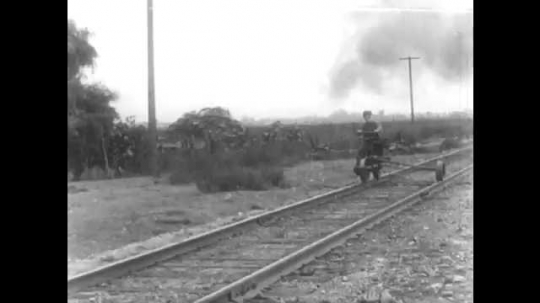 1910s: Boy on pushcart moves cart off of track. Train suddenly comes up to pass him. Man leans from side of train. Trains pass each other on tracks. Boy walks over to man on ground. 