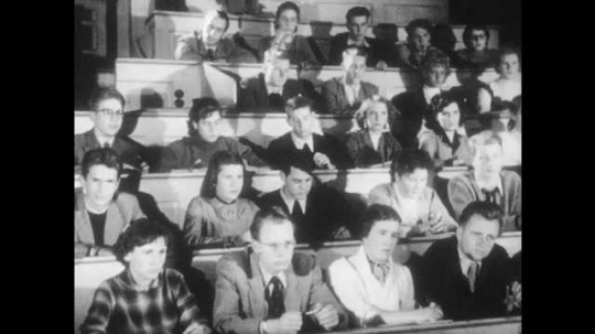 1950s: Students sit in lecture hall. Baby tries to grab toy from hand that moves in front of baby. A man drunk tries to open door. Hand tries to fit a key in door lock, after several tries succeeds.