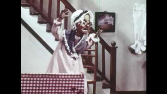 1940s: Animation of grandmother who runs through house to outside. Her scarf and hat fall, she runs away. Wolf comes out, picks up scarf and hat, returns inside. Red Riding Hood arrives at front door.