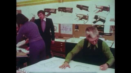 1980s: Tracking shot of draftsmen working in room. Opening title. 