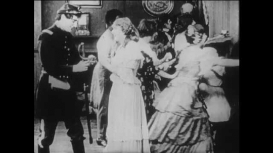 1910s: men and woman celebrate as Northern soldiers parade past house as man in Union soldier uniform walks with girl in dress to grass lawn, sit on stones, hold hands, stand up and enter house.
