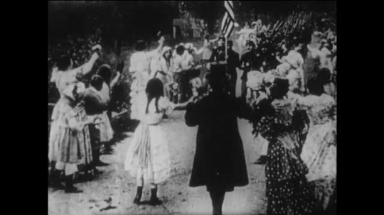 1910s: women, men, boys and girls line sides of street, cheer and wave as Union army soldiers parade with USA flag, drummers, swords, rifles, fifes, backpacks and horse riders. 