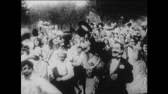1910s: men, woman, girls and boys stand in street and wave hats. woman holds cloth, shuts and cries against door in living room. Title card about battle outside house.