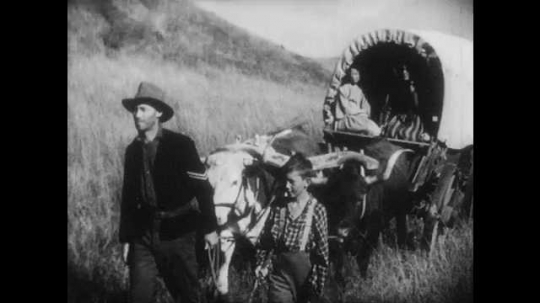 1940s: Man and boy lead bulls pulling wagon across field. Man on horse rides up, talks to man. 