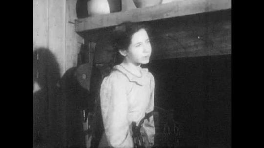 1940s: Sister helps with stew cooking over fire. Father enters cabin with man carrying a bundle. Sister eyes the bundle. 