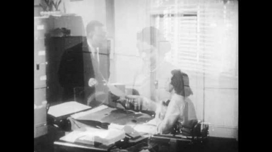 1950s: UNITED STATES: man speaks to lady at desk. Receptionist speaks to client