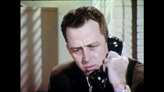 1960s: Man speaks into telephone. Man with glasses sits behind desk and responds into telephone.