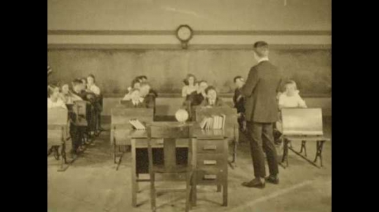 1920s: Teacher is talking to children in classroom. Title card appears. Run down school yard. Cleaned up school yard. Children in class shake heads. Title card appears over building with pillars.
