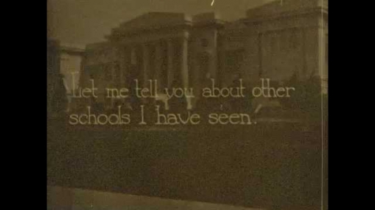 1920s: White building with dark trim. Student go into large school building. Large, white school building with pillars. Teacher talks to class. Title card appears.