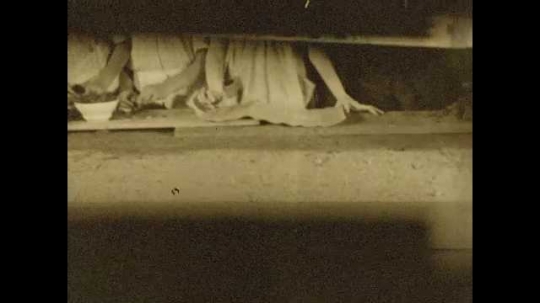 1920s: Teacher places diorama of building on table, surrounded by students.