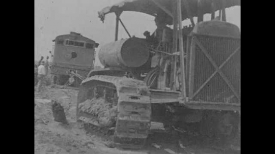 1920s: A tractor pulls a locomotive that jumped the track out of a ditch while me walk alongside, guiding it.