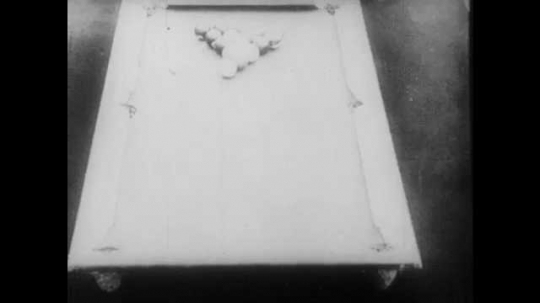 1910s: A pool rack breaks. The balls move around the table and return to their original formation. The crowd congratulates the man who took the shot. A second man steps up to the table to take a shot.