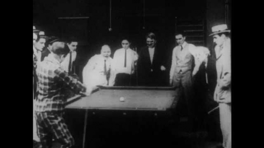 1910s: A crowd celebrates at a pool hall. Intertitle reads, 