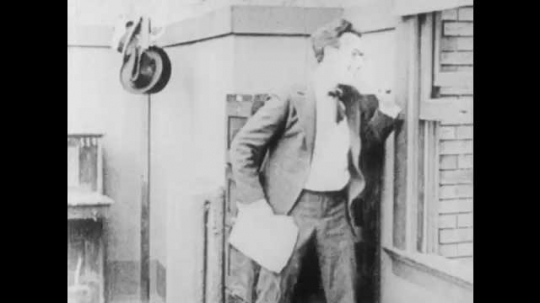 1910s: Women run around trees. Man leans against window and rips papers. Coworker taps boss on shoulder. Boss shakes head and speaks. Text placard. Boss reprimands man and yanks him across room.