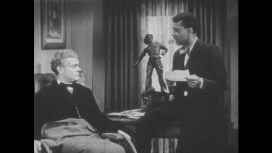 1940s: Booker puts letter on desk and talks to man in wheelchair.