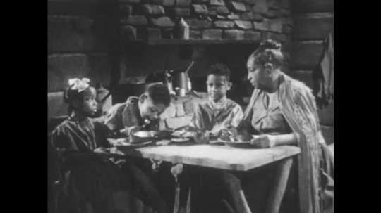 1940s: Slave family sits at table. Woman speaks to children at table. Children respond to woman. Women and children speak at table.