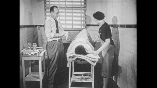 1950s: Doctor dons rubber gloves. Nurse helps woman place feet in ...